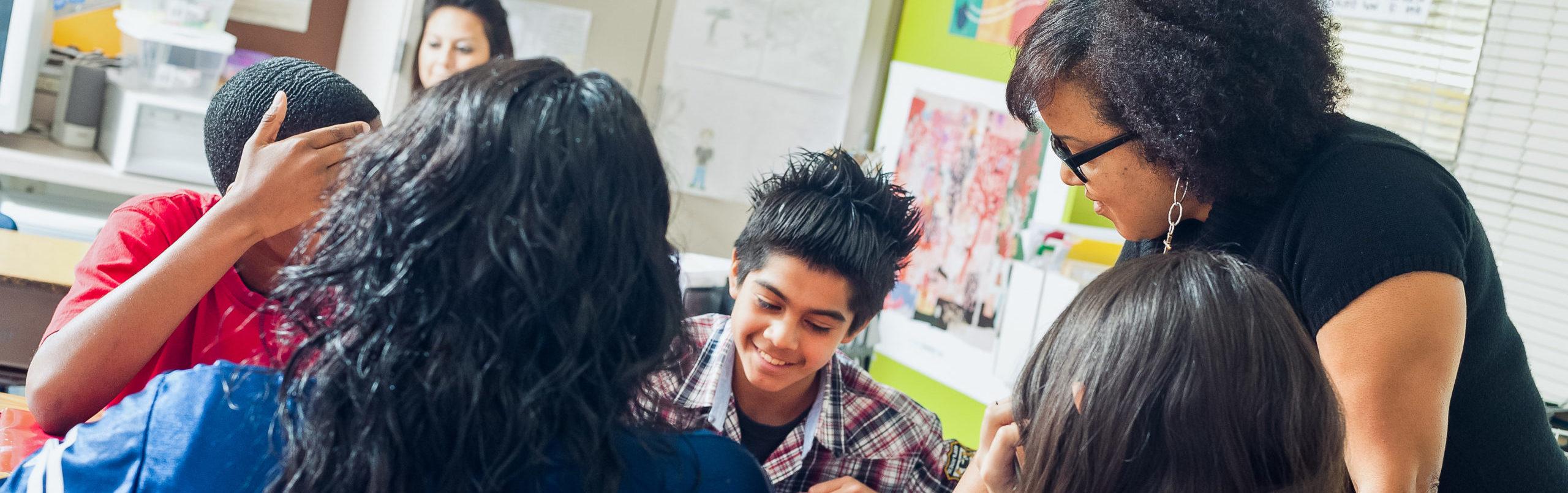 Female teacher working with high school students sitting in desk facing one another