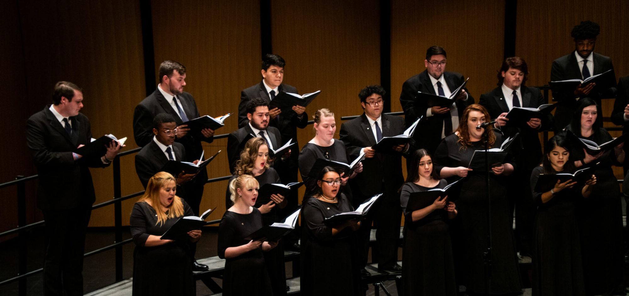 Choir performing on stage wearing formal attire.