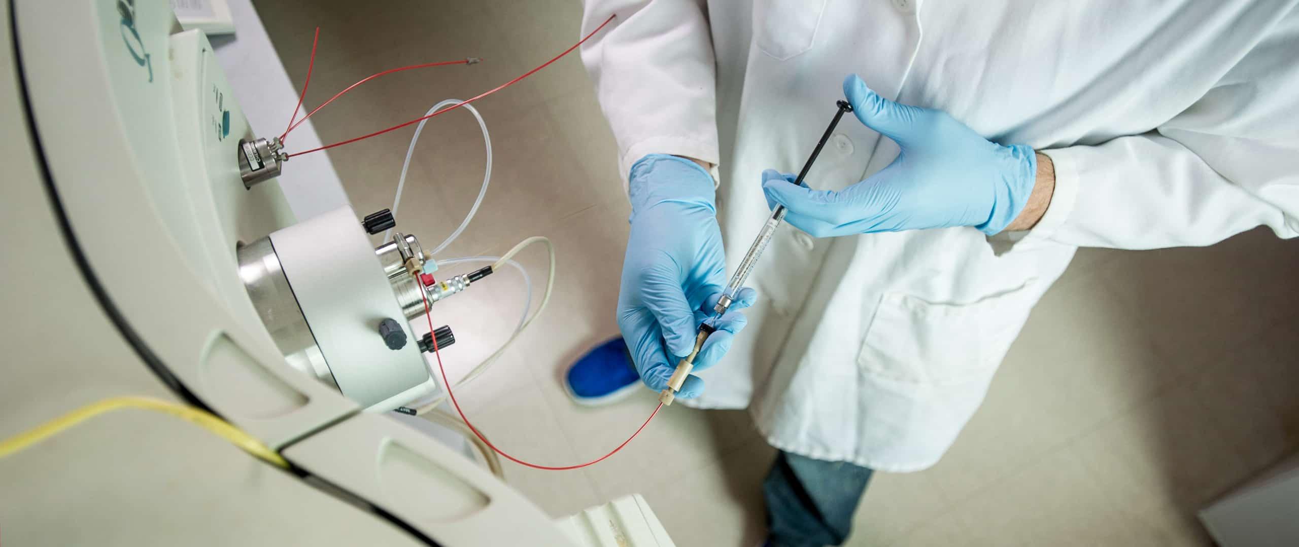 Chemist with personal protective equipment injecting a fluid into a machine