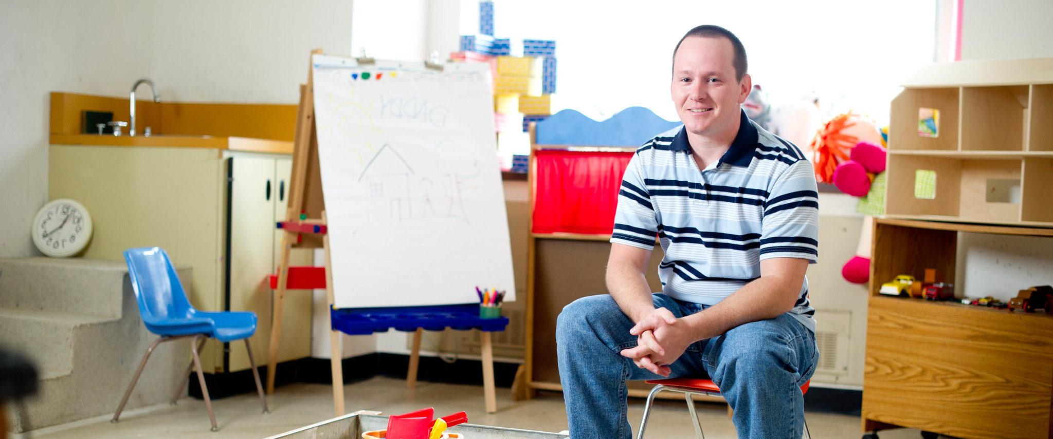 Man sitting by a sandbox in a classroom.