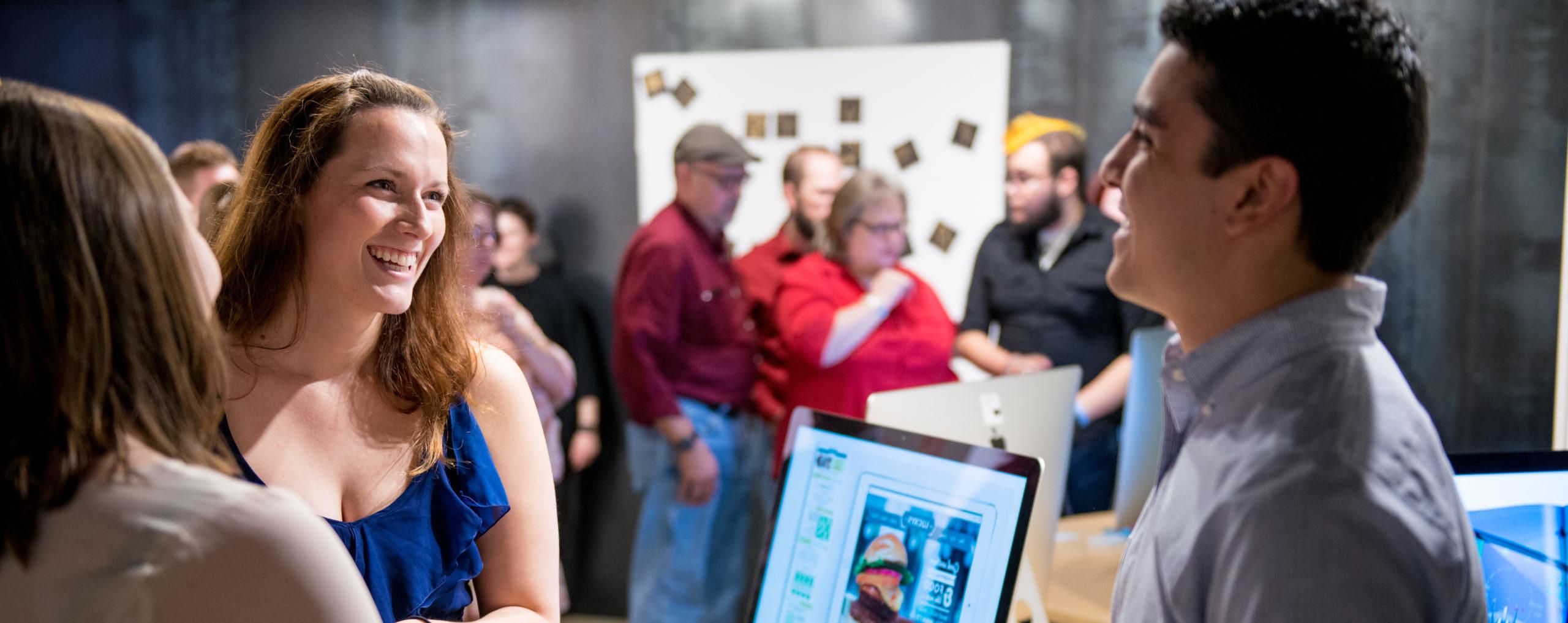 man speaking to two women with computer in gallery setting