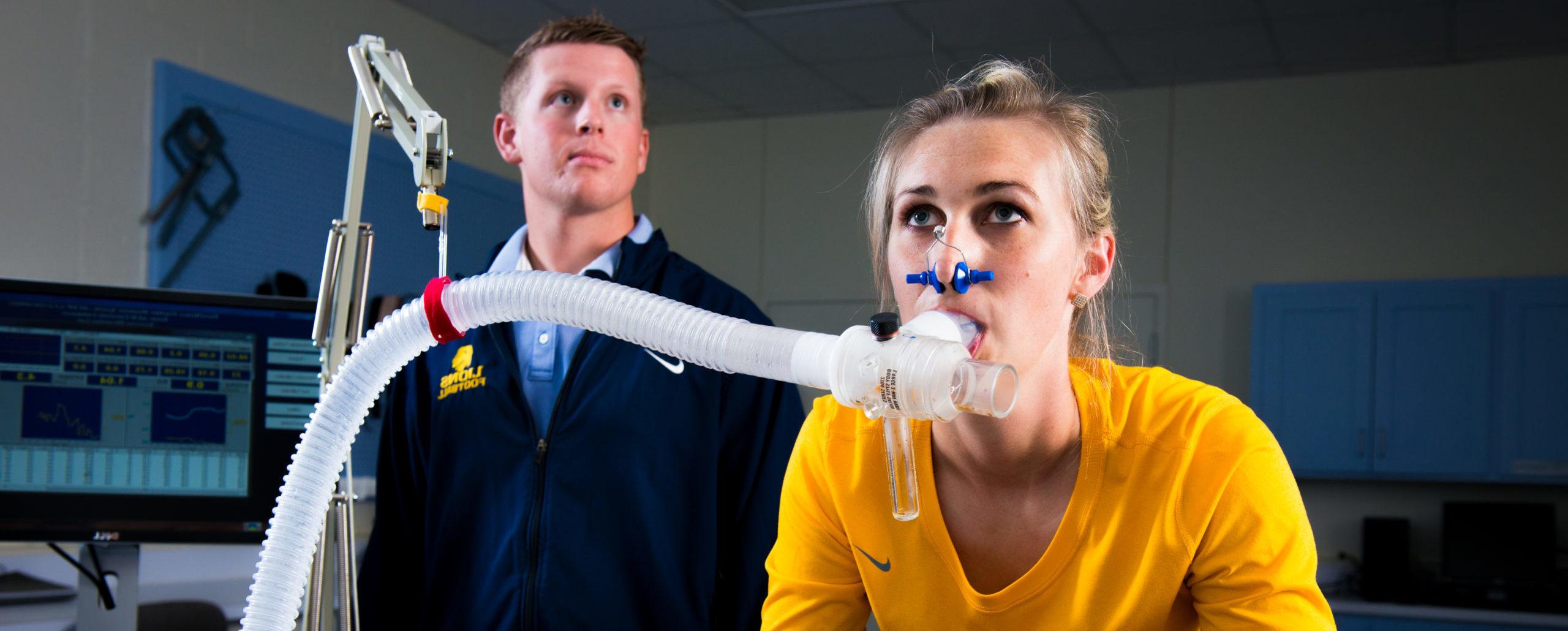 Young lady on exercise bike with ventilator tube measuring oxygen levels.