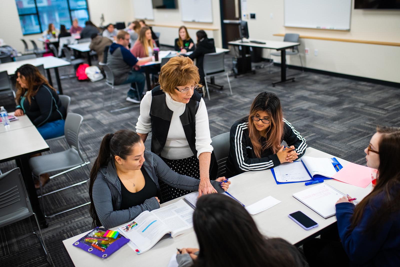 Female instructor working with two young women at a classroom desk.