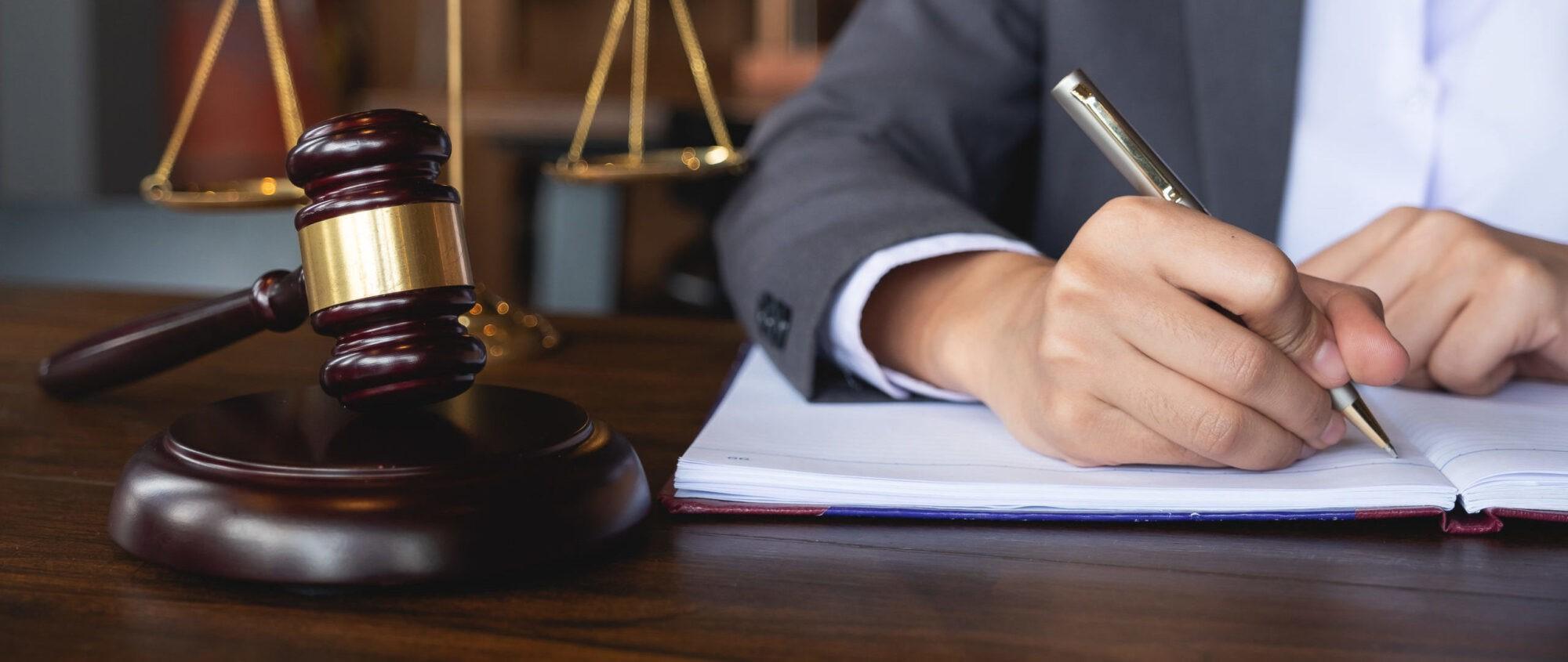 A person writing in a journal beside a judge hammer.