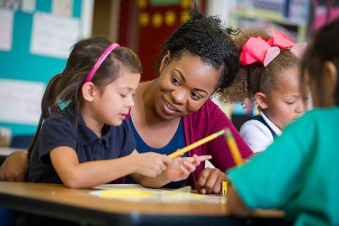 Female teacher with elementary age girl at school desk.