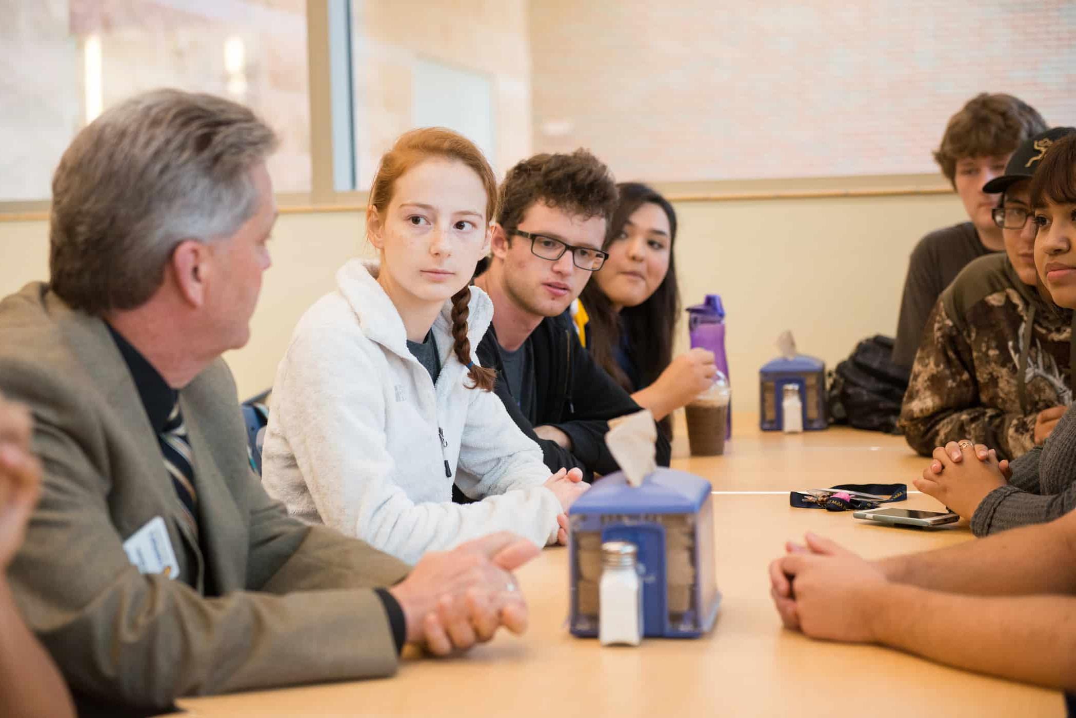 Students sitting together at long table with a professor