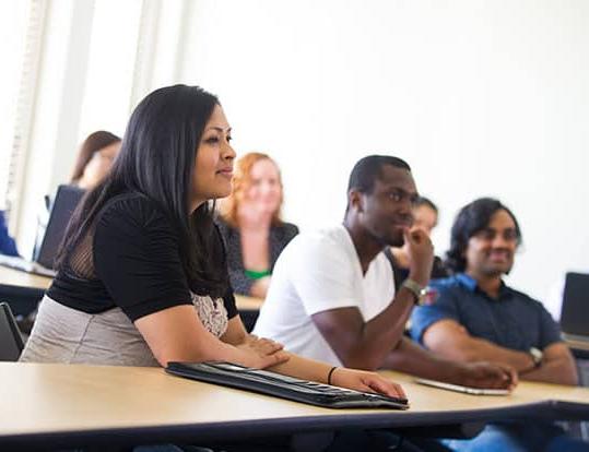 Students in class sitting down at desks listening to lecture.