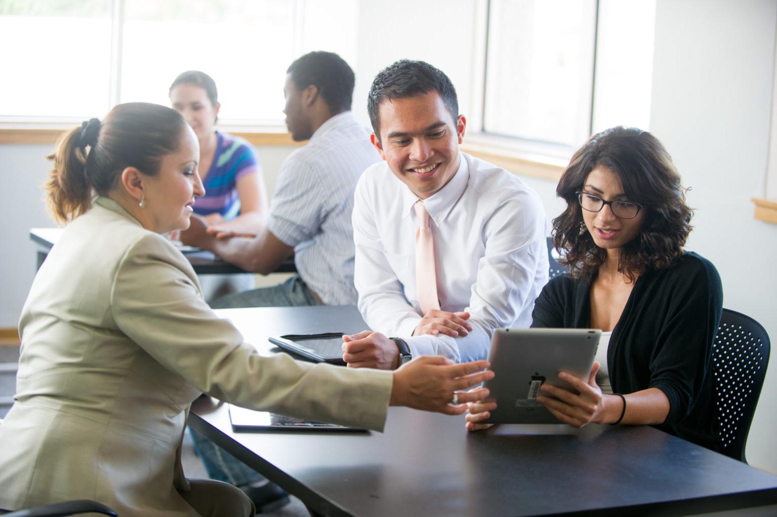 professionally dressed college students working together on a tablet.