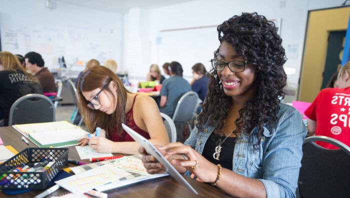 Young African American woman working on tablet in a classroom of college students.