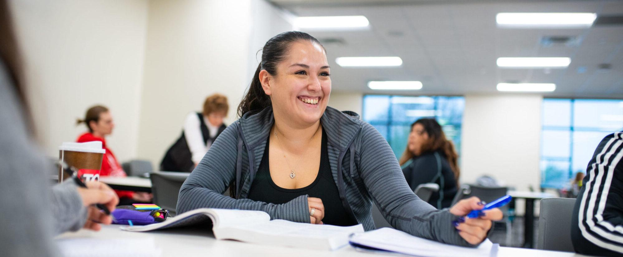 Woman smiling with pen and books in front of her.