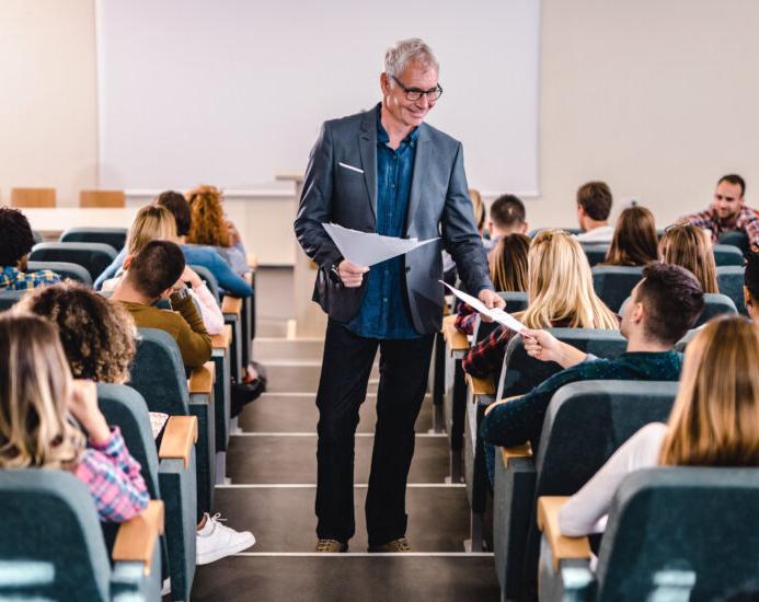 Happy senior professor talking to his students while giving them test results in lecture hall.