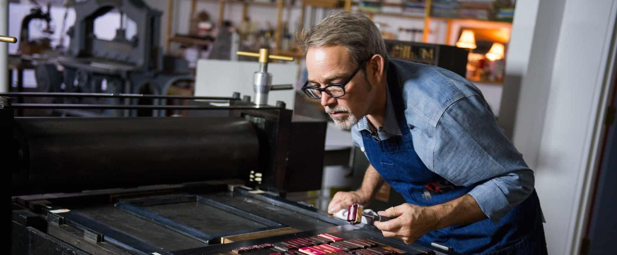 Man working on letter press for art project.