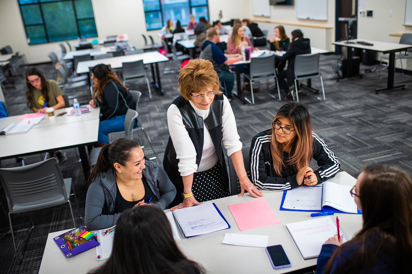 A female professor talking to a group of student sitting down in class.