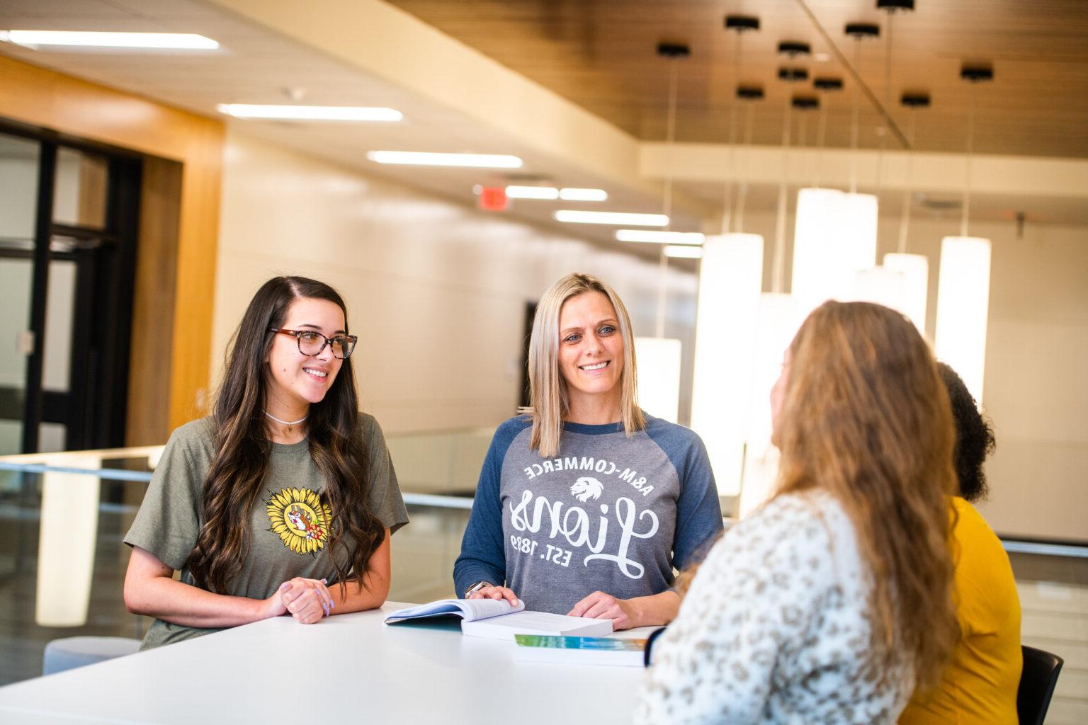 A group of 4 females talking while sitting down at a high desk.