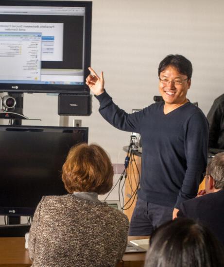 Man pointing to large computer screen while teaching class.