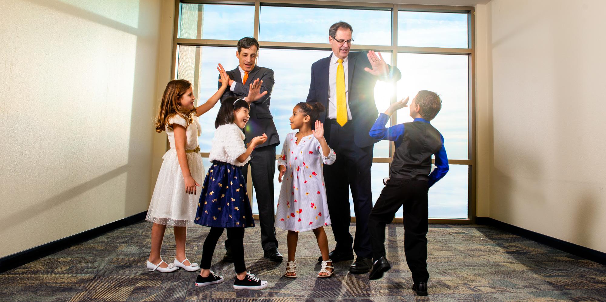 Two professionally dressed men giving high-fives to 4 young kids.