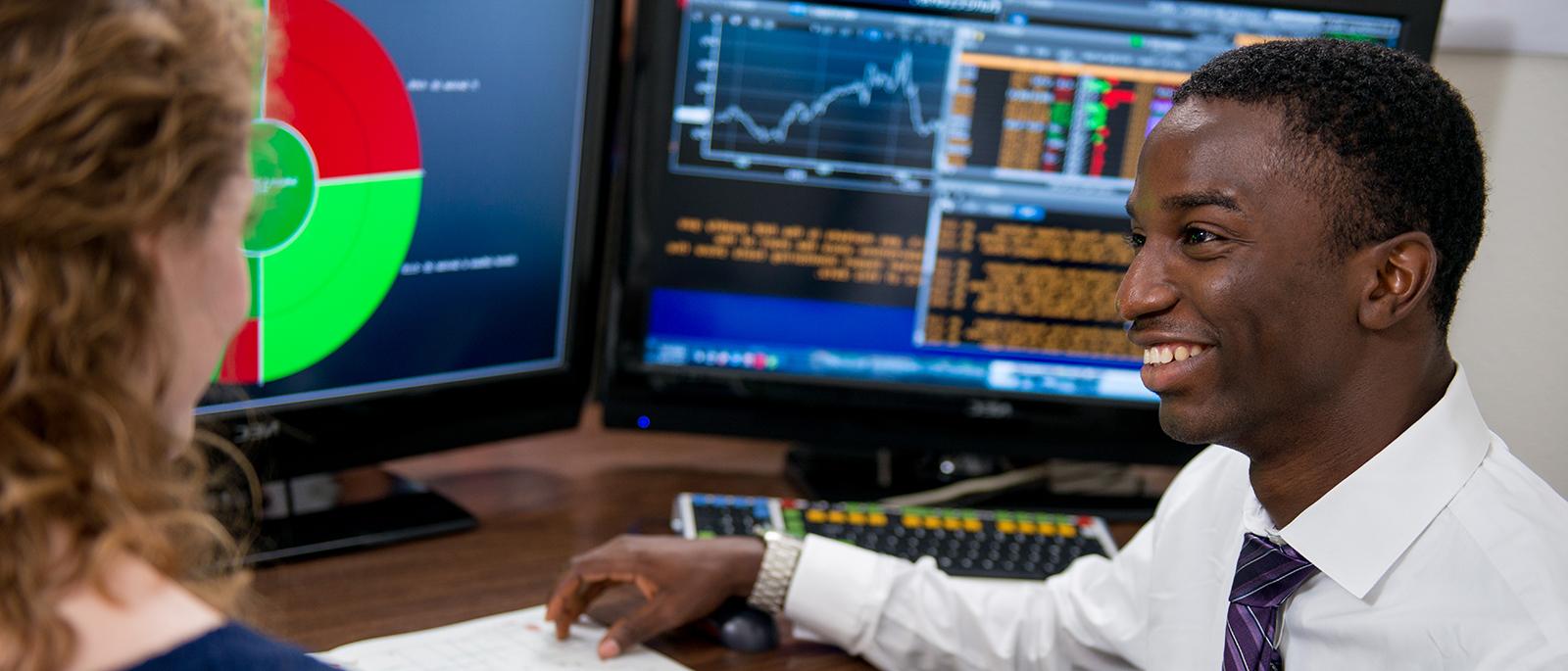 Analyst talking to another professional, with computer screens in the background.