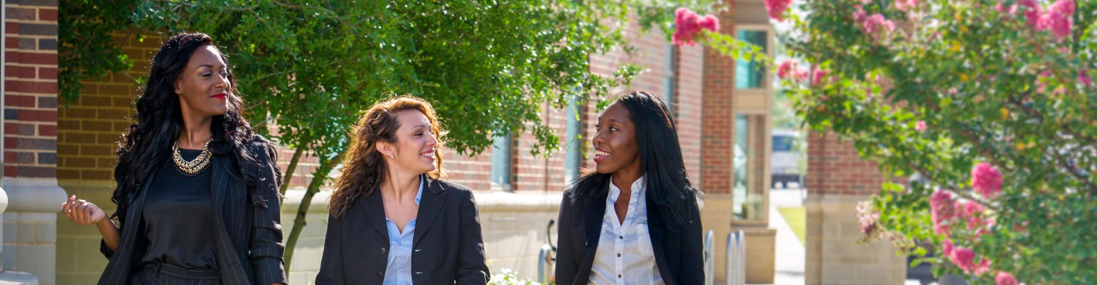 Three women walking together wearing professional attire.