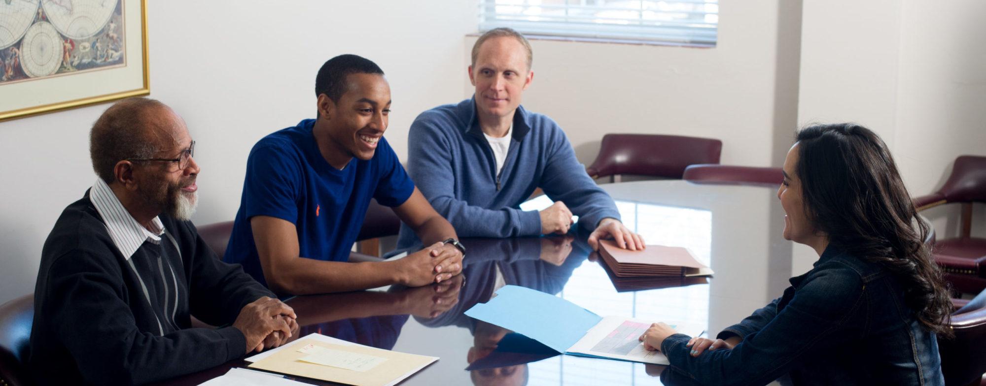 woman with three men discussing files around conference table