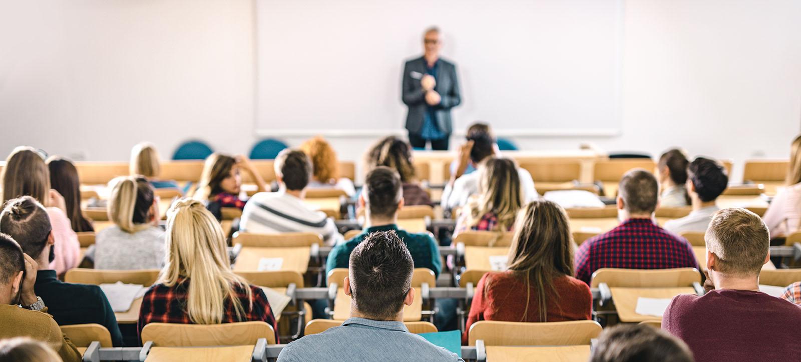 Back view of large group of students paying attention on a class at lecture hall.