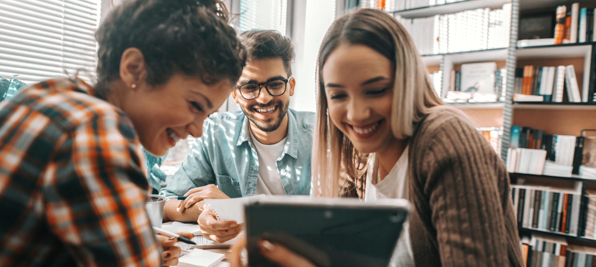 Three student viewing a tablet all smiling.