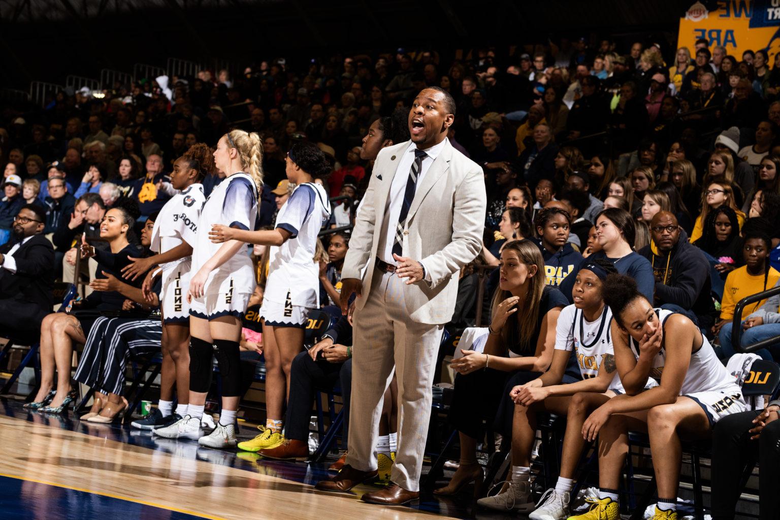 Women's basketball coach standing in front of bench coaching during game.