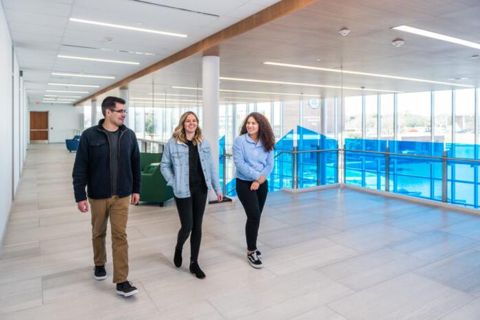 Three students walking in atrium space on second floor.