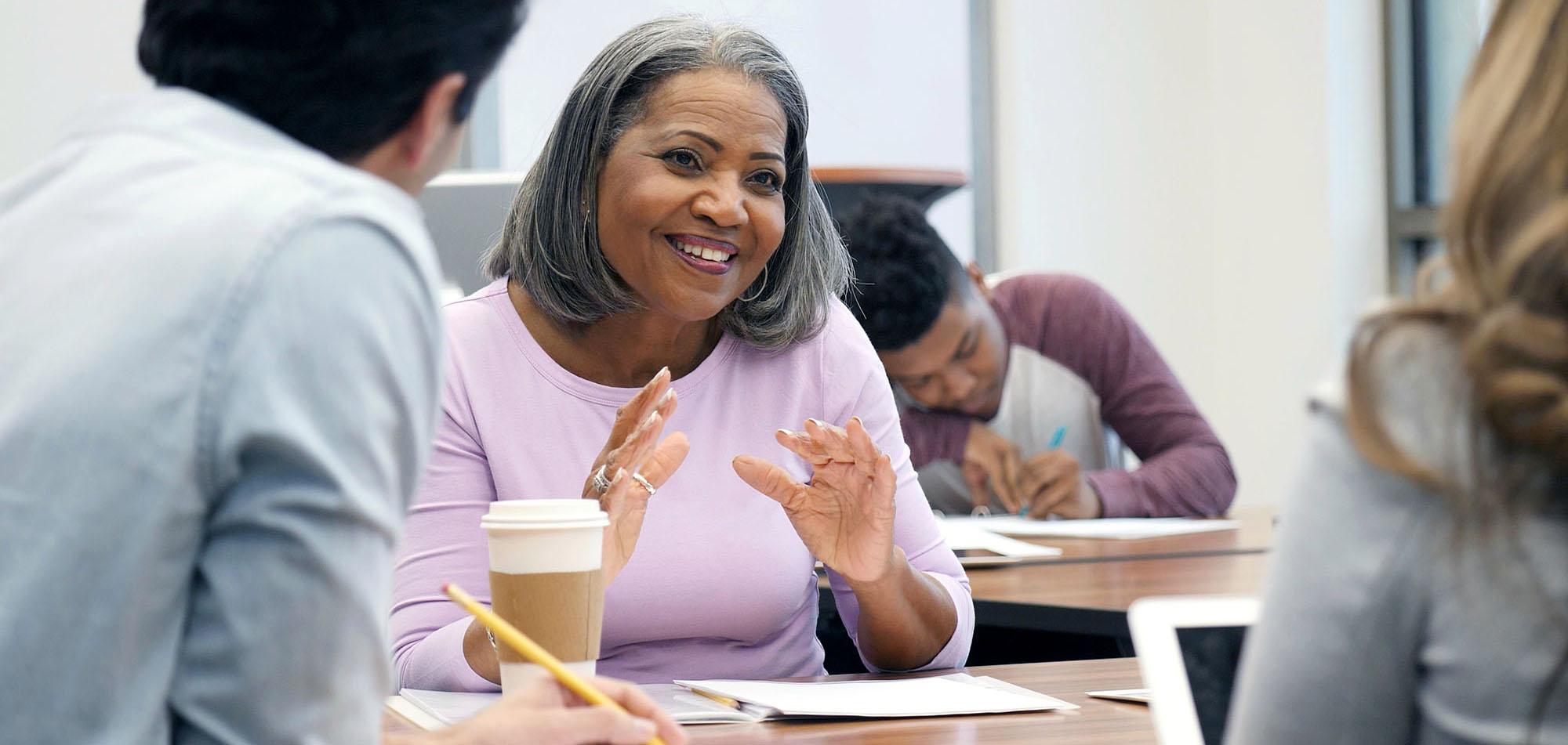 Beautiful mature African American female college student gestures as she discusses something during a study group session with classmates.