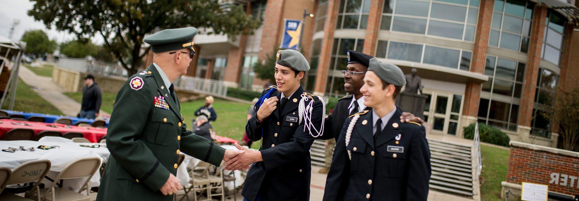 Two young army dressing males are handshaking a male veteran