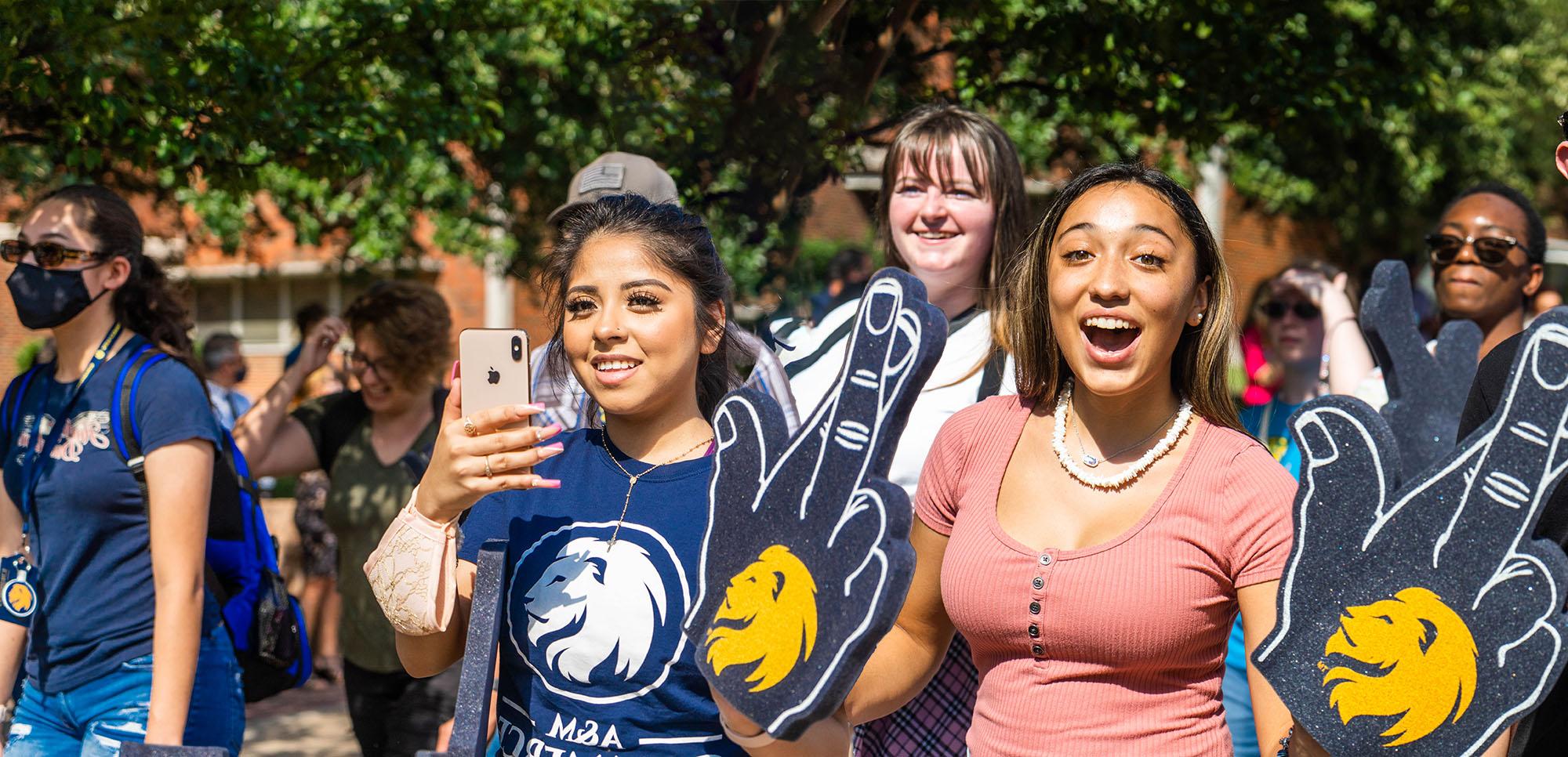 Three female students at the pride walk smiling at the camera with the leo sign.