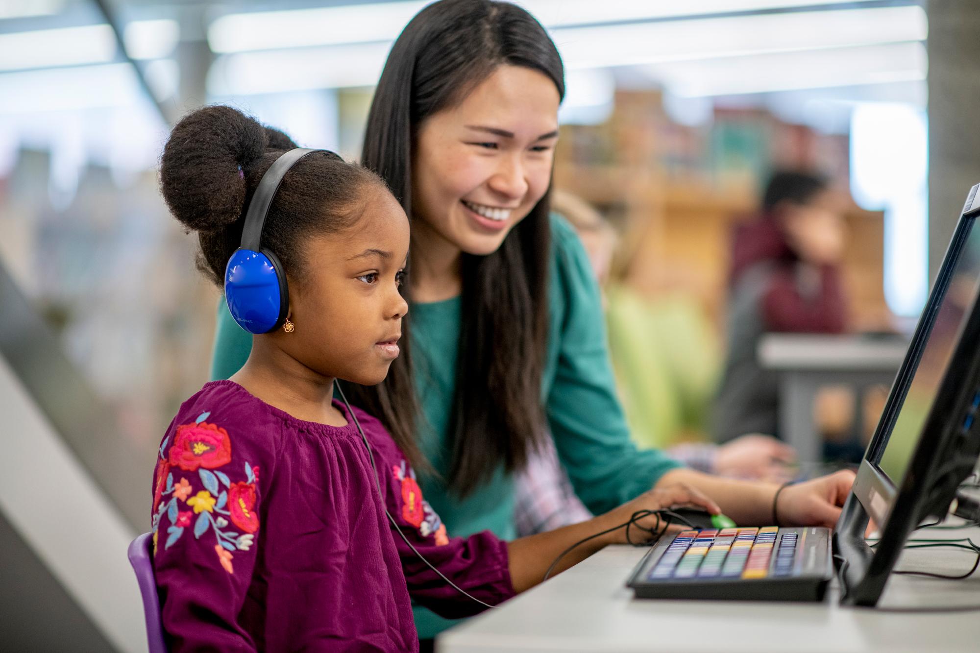 A female teaching student, helping a female enfant on the computer.