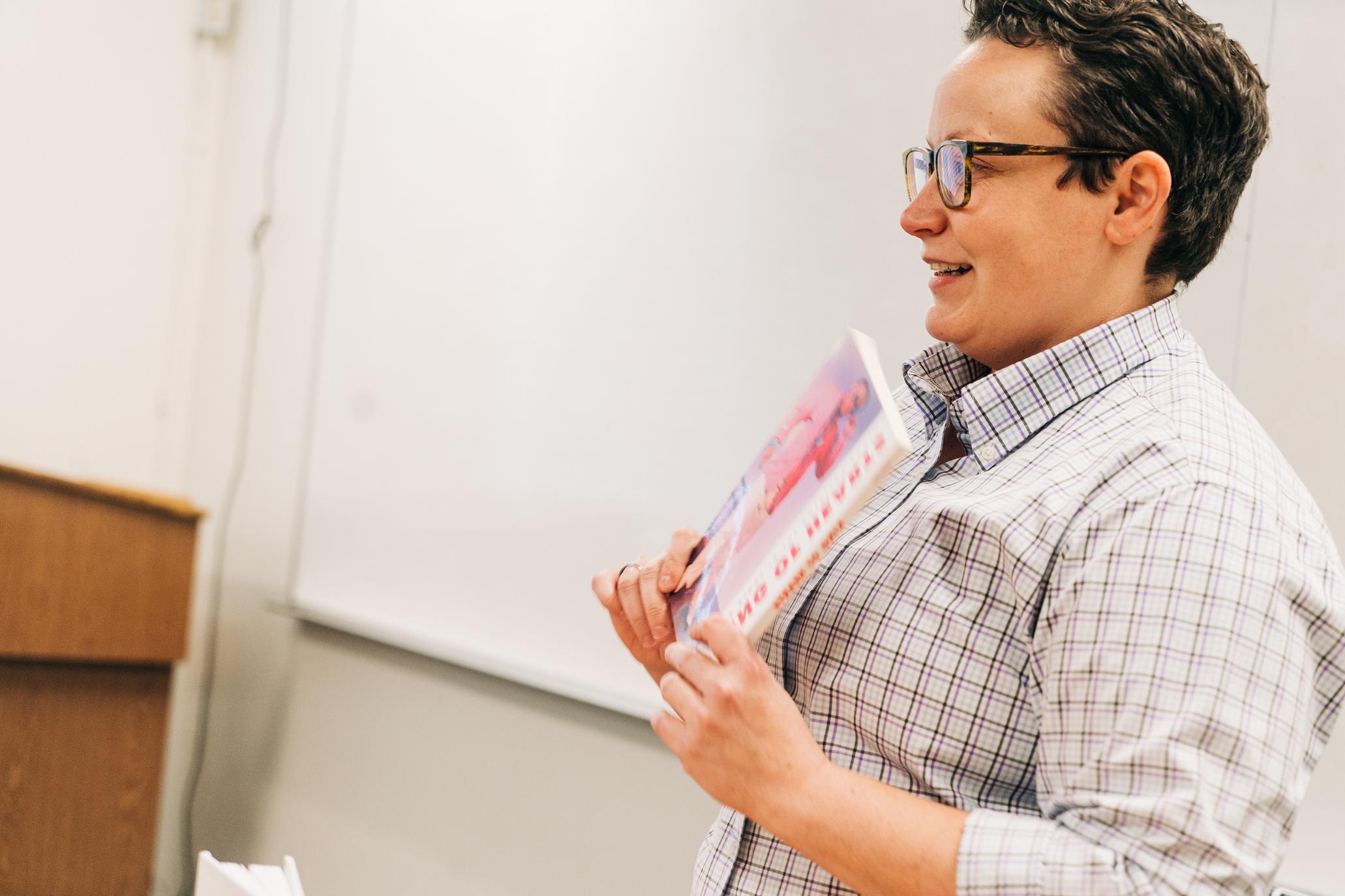 A professor holding a book showing it to the class.