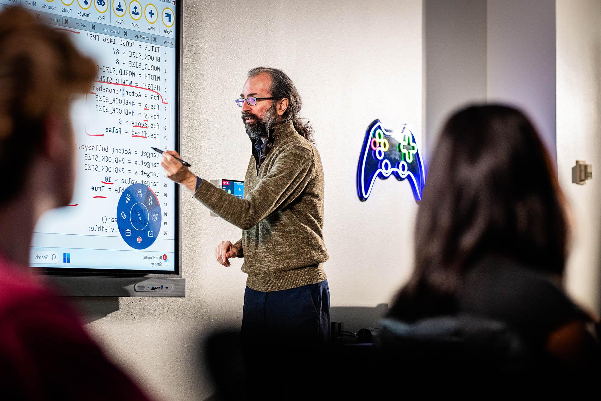 Computer science professor teaching programming concepts on a smartboard during a class at a university.